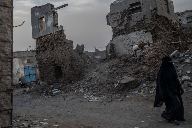 ผู้หญิงคนหนึ่งเดินผ่านซากอาคารในเมืองโมชา ประเทศเยเมน ที่ถูกกบฎฮูตีถล่มเมื่อต้นปี 2560