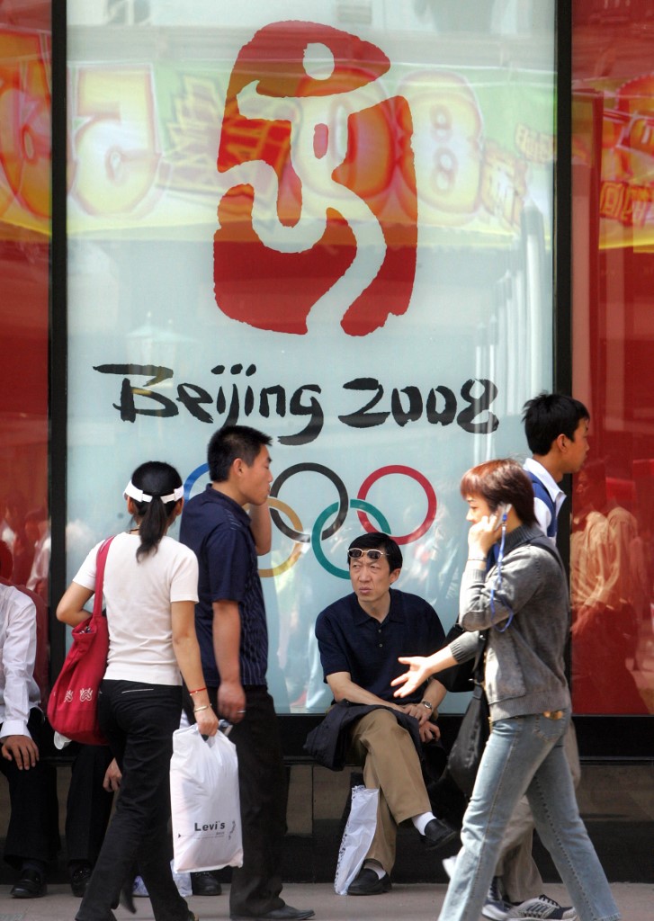 ผู้คนเดินผ่านป้ายที่มีโลโก้โอลิมปิก 2008 ในกรุงปักกิ่ง ประเทศจีน