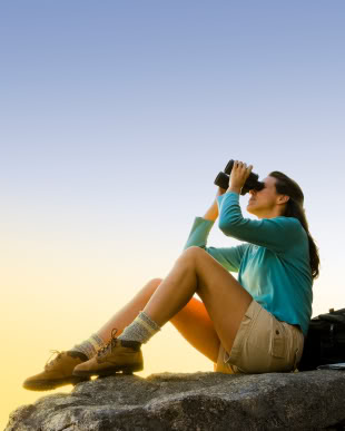 Woman searching with Binoculars on top of mountain.